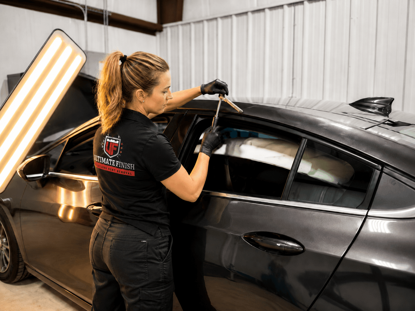 Ultimate Finish technician repairing a vehicle roof panel under shop lighting